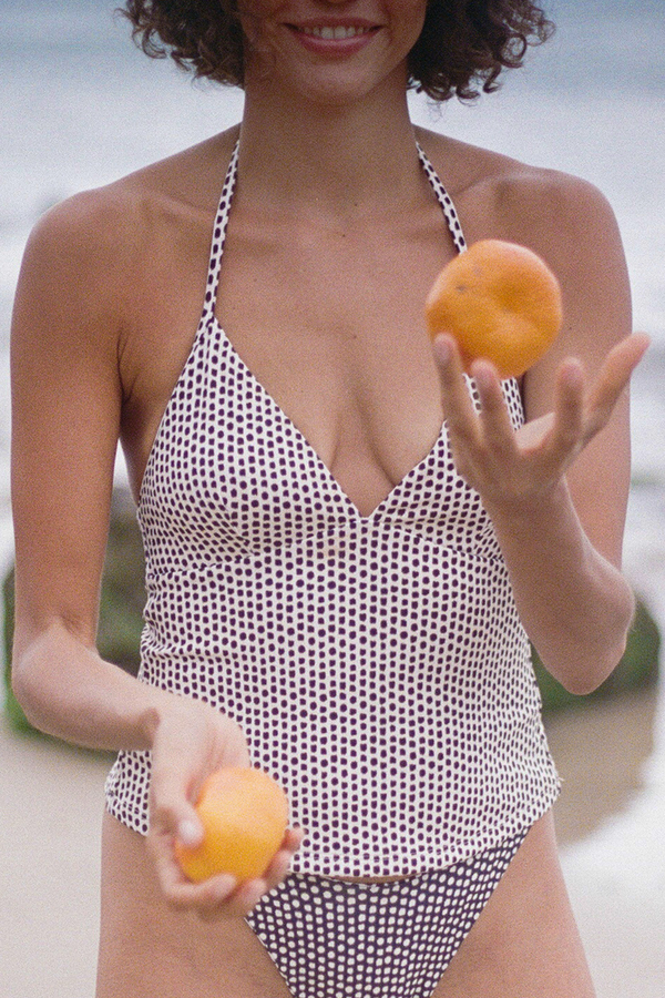 Woman in a black and white patterned swimsuit holding two apricots.